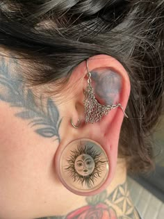 a woman with tattoos on her neck and behind the ear is an ear chain that has a sun design hanging from it