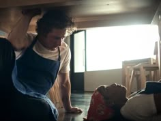 a man in overalls and an apron is leaning over another person on the floor