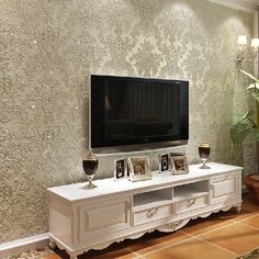 a living room with a large tv on top of a white entertainment center next to a potted plant