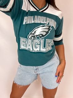 a girl in philadelphia eagles shirt and shorts posing for the camera with her hand up