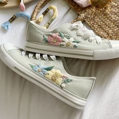 two white shoes with flowers on them sitting on top of a bed next to straw bags