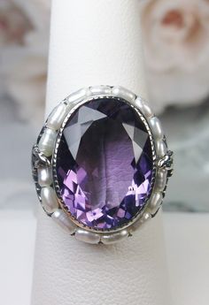 Natural Purple Amethyst & Pearl Ring Leaf Pearl Design#156 This is a stunning 9.5 carat natural purple amethyst gemstone ring. The natural amethyst gem has amazing color and clarity. This gemstone is 12mm x 16mm in dimensions (10/16" x 9/16"). The garden themed filigree circles the edge of the ring and extends down the band accenting the beautiful large gemstone. Seed pearls frame the large gemstone, creating a vibrant contrast. Holding the seed pearls in place are 2 silver leaves and fine w Victorian Style Purple Amethyst Ring For Anniversary, Faceted Purple Amethyst Ring For Formal Occasions, Faceted Amethyst Ring For Anniversary, Exquisite Amethyst Ring For Anniversary, Exquisite Amethyst Ring, Exquisite Amethyst Ring For Wedding, Purple Faceted Wedding Rings, Oval Purple Amethyst Ring, Exquisite Oval Purple Ring