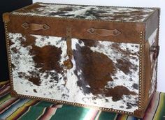 a brown and white cowhide trunk sitting on top of a colorful blanket