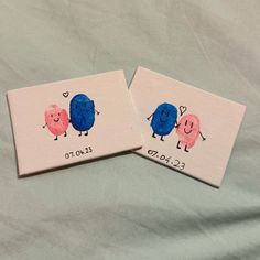 two small cards with faces painted on them sitting on a white sheet, one is blue and the other is pink