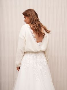 a woman in a white wedding dress standing against a wall with her back to the camera