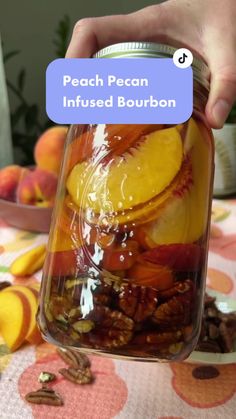 a person holding a jar filled with fruit and nuts on top of a colorful table cloth