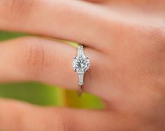 a woman's hand with a diamond ring on top of her finger, showing the center stone