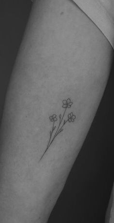 a small flower tattoo on the left inner forearm and arm, with tiny flowers growing out of it