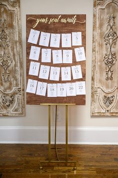 a wooden calendar on a stand in front of two wall hangings with gold lettering