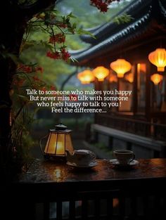 two tea cups sitting on top of a wooden table next to a lit lantern with chinese lanterns in the background