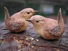 two clay birds sitting on top of a tree stump together with their beaks touching