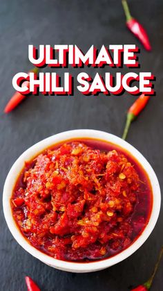 a bowl filled with chili sauce sitting on top of a table next to red peppers