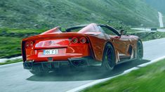 a red sports car driving down a road next to a lush green mountain side field