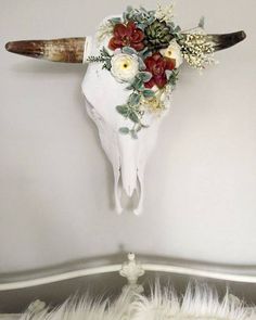 an animal skull with flowers on it's head hanging from the side of a bed