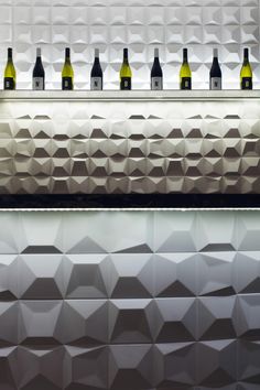 several bottles of wine are lined up on the wall behind an abstract bar counter top