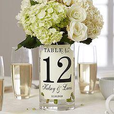 there is a vase with white flowers in it on the table next to wine glasses