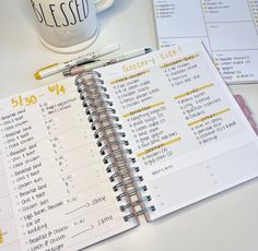 an open planner next to a cup of coffee on a white table with other items