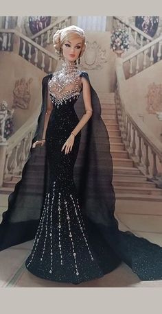 a barbie doll dressed in black and white gown with pearls on her head, standing next to stairs