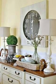 a large clock mounted to the side of a wall next to a lamp and dresser