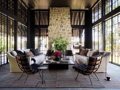 a living room filled with lots of furniture next to tall glass windows on the wall