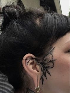 a woman with black ink on her face and ear is looking into the distance while wearing gold hoop earrings