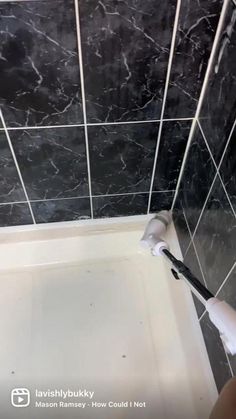 a person using a brush to clean a bathtub with black marble tiles on the walls