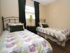 two beds in a bedroom with green curtains and wood flooring, one has a floral comforter on the bed