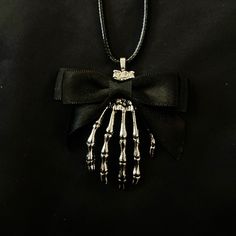 "This is a silver metal pendant featuring a creepy silver metal skeleton hand with a black ribbon bow at the top. It is hung from a black faux leather woven waxed cord that is 19 1/2\" long, with silver chain and a silver lobster claw clasp. Make sure to check out my shop for more hair pins, jewelry, accessories, and all sorts of fun stuff! Skeleton Hand, Black Bow, Bow Necklace, Silver Skeleton Hand, Hand Necklace, Skeleton Necklace, Skull Necklace, Black Ribbon" Alternative Necklaces For Halloween Gifts, Alternative Style Halloween Jewelry As A Gift, Alternative Halloween Gift Necklaces, Black Grunge Necklace For Gift, Grunge Skull Jewelry For Gift, Black Hand Cast Pendant Necklace, Black Skull Necklace For Halloween, Black Skull Jewelry Grunge Style, Black Skull Shaped Grunge Jewelry