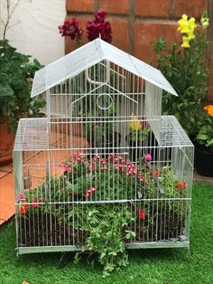 a bird cage with flowers in it sitting on the grass next to potted plants