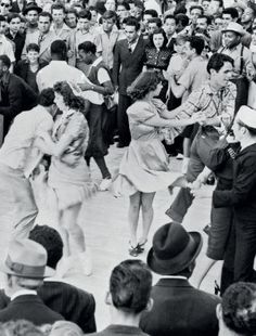 an old black and white photo of several people dancing in front of a large crowd