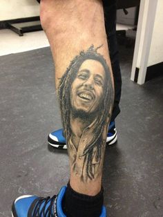 a man's leg with a tattoo of a bob marley smiling and holding his hands together