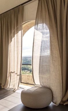 an open window with sheer curtains and a round ottoman in front of it, overlooking the countryside