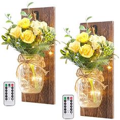 two vases with yellow flowers and lights on them are next to a remote control