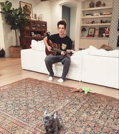 a man sitting on top of a couch next to a small gray dog holding a guitar