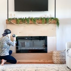 a woman kneeling on the floor in front of a fireplace with a tv above it