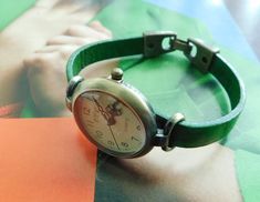 This is a simple women watch with a distressed green leather band. The style is retro minimalist with a distress look. The face of the watch is made in aged bronze finish alloy, free of nickel and lead, round shape 1.25 inches diameter. The band will be make to fit your wrist, please select the measure of your wrist from the list when you buy it.   If you need another size, please send me a message. The clasp is fold-over and is made in metal alloy with also bronze finish. Comes with and extra b Classic Green Watch For Everyday Use, Trendy Green Watches As Gift, Everyday Green Quartz Watch, Modern Green Watch With Bracelet Strap, Handmade Adjustable Green Watch Bands, Green Watches With Leather Strap And Round Dial, Green Leather Analog Watch, Green Leather Watches With Subdials, Classic Green Leather Watch Band