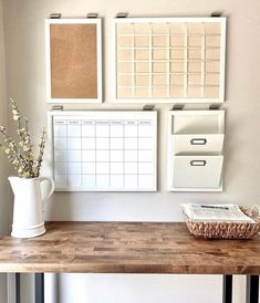 a wooden table topped with a white vase filled with flowers next to a wall mounted calendar