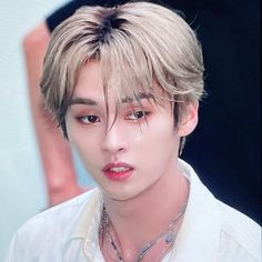 a young man with blonde hair wearing a white shirt and silver necklace on his neck