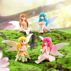 four little fairy figurines sitting on top of a green field with pink flowers