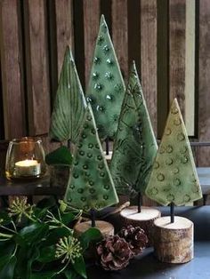 three green trees sitting on top of a table next to some pine cones and candles