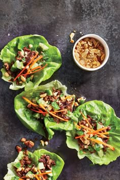 lettuce wraps with meat, carrots and nuts on a black surface next to a small bowl