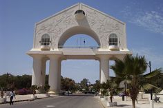 a large white building with an arch on the side and palm trees in front of it