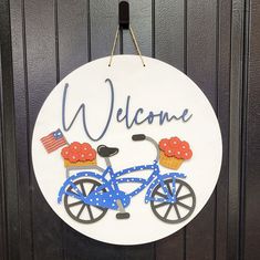 a sign that says welcome with a bicycle and cupcakes on the front wheel