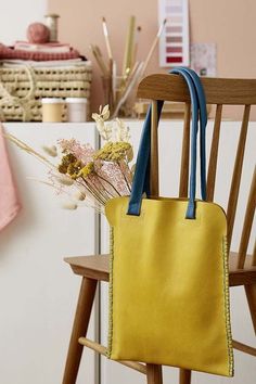 a yellow purse sitting on top of a wooden chair next to a vase with flowers