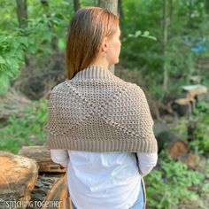 a woman standing in the woods wearing a knitted shawl and looking at trees