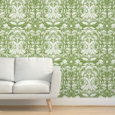 a white couch sitting in front of a wall with green and white designs on it