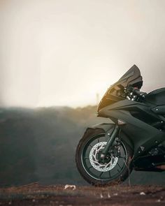 a black motorcycle parked on top of a dirt road next to a mountain side with the sun shining down