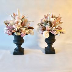 two black vases with flowers in them on a white background