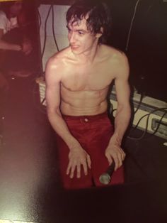 a shirtless man holding a bottle in his right hand while sitting on a stool