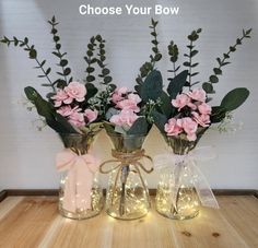 three vases with flowers and lights in them